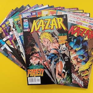 May include: A collection of comic books fanned out against a yellow background. The covers feature vibrant illustrations and text, with titles like "Kazar" and "Marvel." The comic books are in good condition, showcasing colorful artwork and bold lettering.