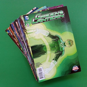 Op de afbeelding: Een stapel stripboeken, waarvan de bovenste Green Lantern toont. De cover van het stripboek is overwegend groen, met het Green Lantern-personage in het midden. Het stripboek is getiteld "Green Lantern" en "DC Comics".