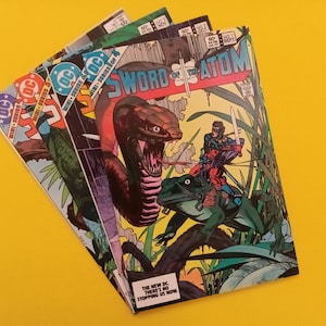 May include: A stack of comic books featuring vibrant illustrations. The top comic book is titled "Sword of the Atom" with a snake and a warrior on a frog. Other comics are visible, with DC Comics logos and issue numbers.