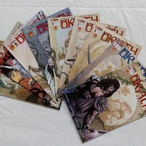 Puede incluir: Una colección de cómics en abanico. Las portadas presentan ilustraciones de fantasía y el título "BRATH". Se ven los números de las ediciones. Dispuestos sobre una superficie blanca.