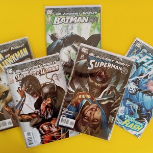 以下が含まれることがあります： バットマン、スーパーマン、ワンダーウーマン、フラッシュ、アトムとホークマンが登場するDCコミックス「Blackest Night」のコミックのコレクション。表紙には鮮やかなイラストとDCコミックスのロゴが黄色い背景に描かれています。