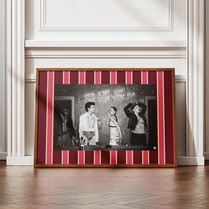 May include: Black and white photograph of four people standing in a room with red and white striped wallpaper. The people are wearing casual clothing and are looking at the camera. The text "Here's to the ones that look like us" is written on the wall behind them.