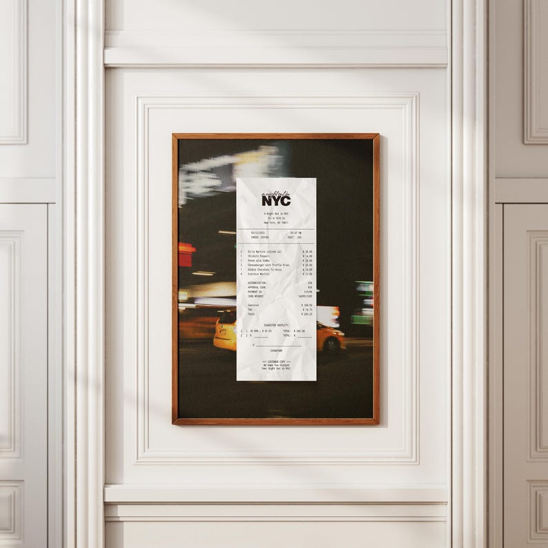 May include: A framed print featuring a receipt with the text "NYC" at the top. The background is a blurred image of a city street at night, with yellow taxi cabs and bright lights. The frame is a warm brown colour.