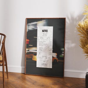 May include: Framed print depicting a blurred night street scene with yellow taxi cabs and a large receipt. The receipt has the text "NYC" at the top. The frame is a dark brown colour.