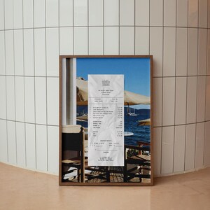 Peut inclure: Une photo encadr&eacute;e d'un re&ccedil;u d'un restaurant appel&eacute; "Olive's Garden" avec une vue sur l'oc&eacute;an et une table avec des chaises au premier plan. Le re&ccedil;u indique les articles command&eacute;s, les prix et le montant total d&ucirc;.