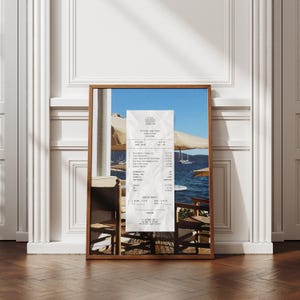 Peut inclure: Un re&ccedil;u du "The Harbor Cafe & Bar" en Gr&egrave;ce, montrant une liste d'articles de nourriture et de boissons avec leurs prix. Le re&ccedil;u est sur une table avec deux chaises, donnant sur une mer bleue avec des bateaux au loin.