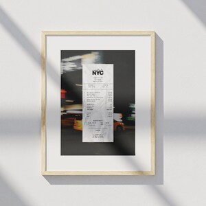 May include: Framed print of an NYC receipt, with the city's logo at the top. The receipt is set against a blurred backdrop of city lights and yellow taxis. The frame is a light wood colour.