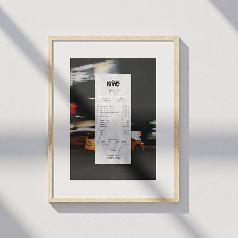 May include: Framed print of an NYC receipt, with the city's logo at the top. The receipt is set against a blurred backdrop of city lights and yellow taxis. The frame is a light wood colour.