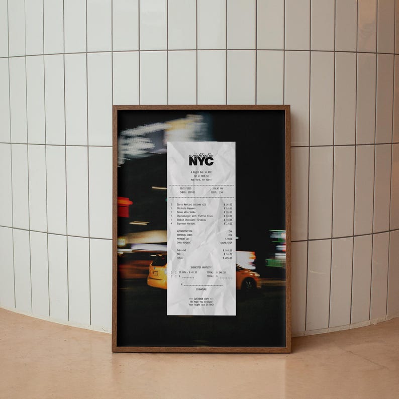 May include: A framed print showing a crumpled NYC receipt against a blurred cityscape. The receipt has black text on white paper, and the frame is dark wood. The background features yellow taxis and street lights.