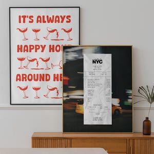 May include: Two framed art prints. One has red text saying "IT'S ALWAYS HAPPY HOUR AROUND HERE" with cocktail illustrations. The other is a photo of a NYC receipt.