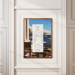 Peut inclure: Une impression encadr&eacute;e d'un re&ccedil;u du restaurant The Beach House en Gr&egrave;ce. Le re&ccedil;u est sur une table avec vue sur l'oc&eacute;an et des bateaux au loin. Le re&ccedil;u est dat&eacute; du 03-07-2021 et comprend des articles comme la salade grecque, les courgettes frites et une bouteille de vin.