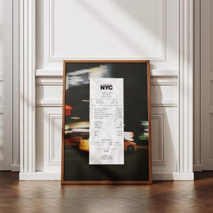May include: A framed print showing a blurred night street scene with yellow taxis and a large receipt. The receipt, with "NYC" at the top, lists itemized costs. The print is in a wooden frame.