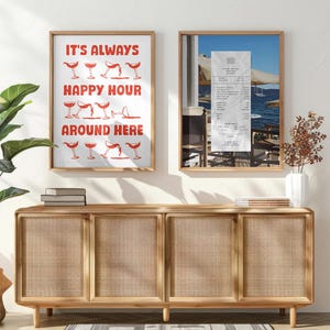 Peut inclure: Deux impressions encadr&eacute;es sur un mur blanc au-dessus d'un meuble en bois avec des portes en rotin tiss&eacute;. L'impression de gauche dit "It's Always Happy Hour Around Here" avec une illustration rouge de verres de vin. L'impression de droite montre un re&ccedil;u et une vue d'une terrasse de restaurant.