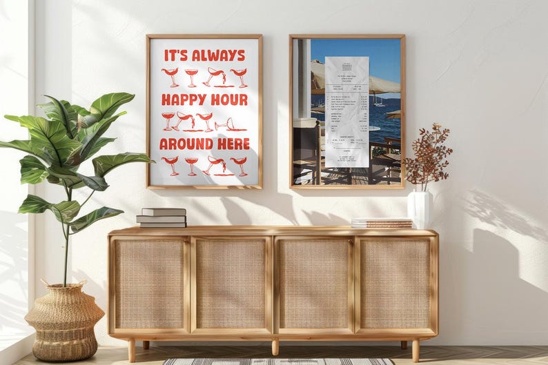 Peut inclure: Deux impressions encadr&eacute;es sur un mur blanc au-dessus d'un meuble en bois avec des portes en rotin tiss&eacute;. L'impression de gauche dit "It's Always Happy Hour Around Here" avec une illustration rouge de verres de vin. L'impression de droite montre un re&ccedil;u et une vue d'une terrasse de restaurant.