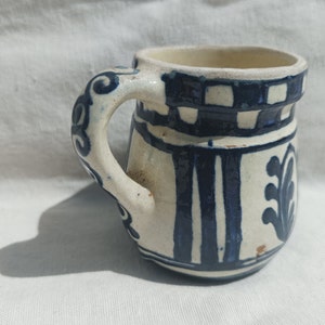 Peut inclure: Une tasse en céramique blanche avec un motif géométrique bleu et blanc. La tasse a une anse avec un design décoratif.