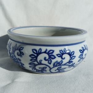 Op de afbeelding: Een witte keramische kom met een blauw en wit bloemenpatroon. De kom is rond en heeft een brede rand.