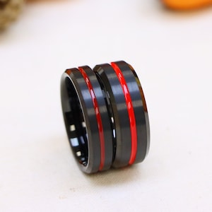 May include: Two black tungsten carbide rings with red inlay lines. The rings are stacked on top of each other.