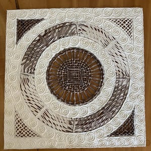 May include: A square wall art piece featuring a white raised spiral pattern on a textured background. The center contains a dark brown woven circular design with a square motif. Four dark brown triangular woven patterns occupy the corners.