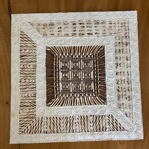 May include: A square wall art piece featuring a central woven grid of brown and tan fibers surrounded by a border of textured, light-colored natural materials. The outer frame consists of a white, raised spiral pattern on a square base.