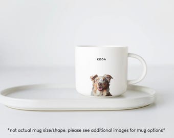 May include: White ceramic mug with a brown and white dog on it. The dog is looking at the camera and has the name "KODA" printed on the mug.