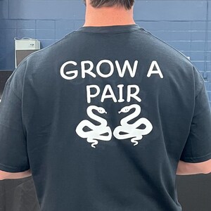 May include: Black t-shirt with white text that reads "Grow a Pair" and two white snakes facing each other.