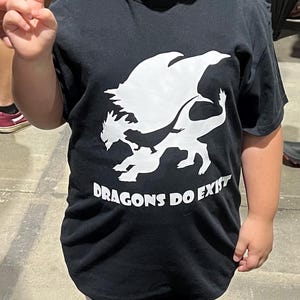 May include: A black t-shirt with a white silhouette of a dragon and the text "DRAGONS DO EXIST".