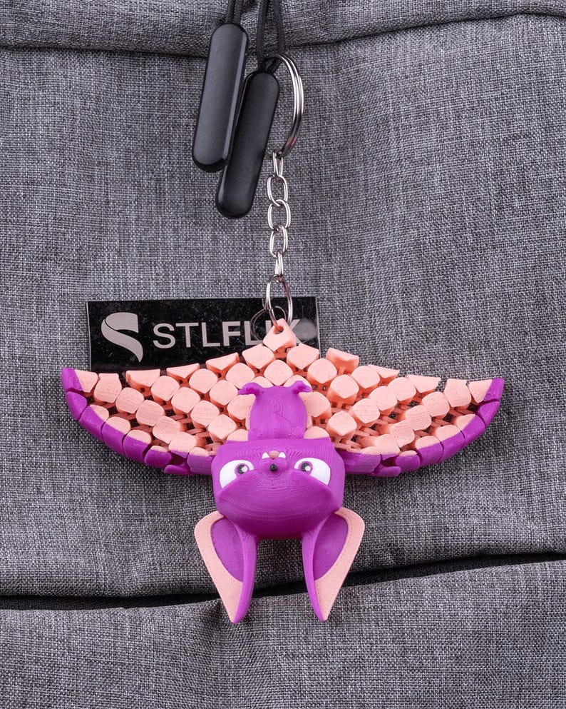 May include: A purple and pink 3D printed bat keychain with a STLFLX logo tag. The bat is hanging from a silver chain.