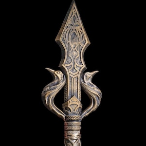 May include: An ornate bronze spearhead with detailed carvings and a pointed tip. The spear features stylized bird-like figures on either side of the shaft. The spear is set against a black background, highlighting its intricate design.