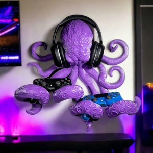 May include: A purple octopus-shaped wall mount holding black headphones and video game controllers. The octopus has textured skin and holds controllers in its tentacles. A blue controller is also visible.