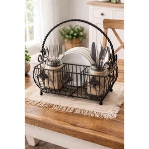 May include: A black wrought iron flatware and plate caddy with a handle. The caddy has two jars wrapped in burlap for utensils and a section for plates. The caddy is decorated with leaf accents and sits on a beige placemat.