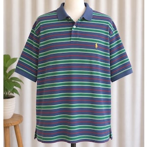 May include: A blue polo shirt with horizontal stripes in green, red, and white. The shirt has a blue collar and short sleeves. A small yellow logo is on the left chest.