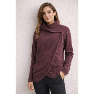May include: A burgundy wrap-style long-sleeve top with a high collar. The top has a diagonal seam across the front and a pocket on the left side. The model is wearing black pants. The top is made of a soft, textured fabric.