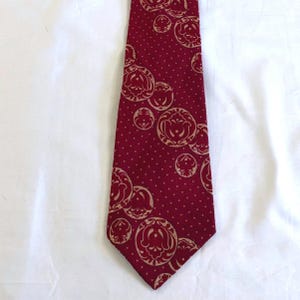 May include: A burgundy tie with a repeating pattern of beige floral medallions and small white dots. The tie is made of a smooth fabric and is suitable for formal or business attire.