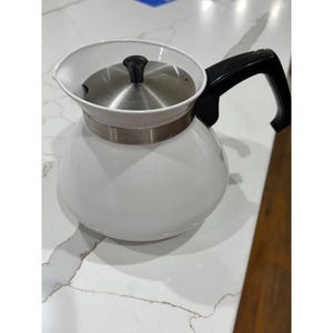 May include: A white glass coffee pot with a stainless steel lid and a black handle. The pot has a rounded body and a white rim. The handle is curved and attached to the side of the pot. The lid has a black knob.
