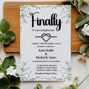 May include: A wedding invitation with a white background and green foliage border. The text reads "Finally, We are tying the knot" with a black rope knot and heart. The invitation is for Kara Smith and Kimberly Jones, and the ceremony will be held at 4 o'clock in the afternoon at the Pavilion at Central Market in Charleston, South Carolina. A reception will follow.