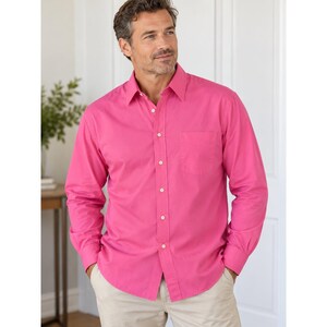 May include: A long-sleeved button-down shirt in a vibrant hot pink colour. The shirt features a classic collar, a single chest pocket on the left side, and white buttons running down the centre placket and on the cuffs of the long sleeves.