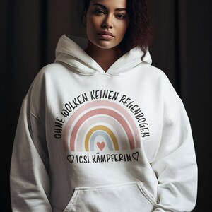 Peut inclure: Sweat-shirt à capuche blanc avec un motif arc-en-ciel et le texte "Ohne Wolken keinen Regenbogen" et "ICSI Kämpferin" en noir.
