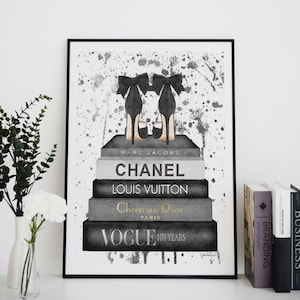 May include: A framed wall art print featuring a stack of five books labelled Marc Jacobs, Chanel, Louis Vuitton, Christian Dior Paris, and Vogue 100 Years. Atop the books are two black high-heeled shoes with bows, set against a white paint-splattered background.