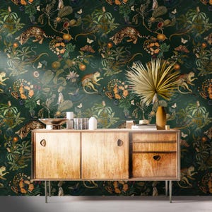 Pode incluir: Um armário de madeira com um design moderno de meados do século, com um fundo de papel de parede verde escuro com tema de selva. O papel de parede apresenta macacos, tigres, borboletas e várias plantas em tons de verde, laranja e castanho.