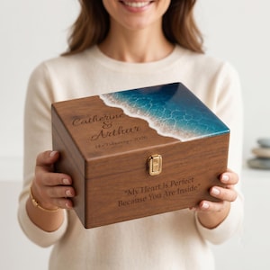 May include: A rectangular wooden keepsake box with a hinged lid featuring a blue and white resin ocean wave design. The lid is engraved with the names Catherine & Arthur and the date 14 February 2026. The front is engraved with the text My Heart Is Perfect Because You Are Inside.