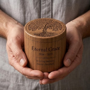 May include: A cylindrical wooden cremation urn featuring a laser-engraved tree of life on the lid. The side is engraved with the text Eternal Grace, the dates 1946-2021, a small heart icon, and the phrase In loving memory, forever cherished.
