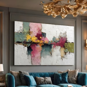 May include: Large abstract painting with a textured white background and colorful vertical and horizontal brushstrokes. The artwork features pink, green, yellow, and dark blue hues, creating a modern and vibrant aesthetic. The painting is displayed above a blue sofa.