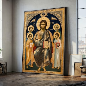 May include: A framed religious icon depicting a central figure with a halo, seated and holding a book. The icon features gold, blue, and brown tones, with figures surrounding the central person. The artwork is displayed against a neutral wall.