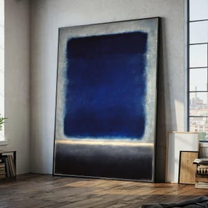 Pode incluir: Grande pintura abstrata emoldurada com um retângulo central azul escuro, ladeado por azul claro e cinza. Uma fina faixa horizontal dourada e cinza separa o azul escuro de uma base preta. A obra de arte está encostada a uma parede.
