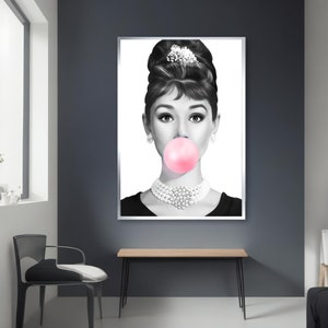May include: Black and white portrait of a woman with a large pink bubble gum in her mouth. She is wearing a pearl necklace and a black dress.
