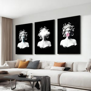 May include: Three framed art prints featuring white busts of Medusa against a black background. One has a cloud, another a bubblegum bubble, and the third has a blue hue. The art is displayed above a white sofa.