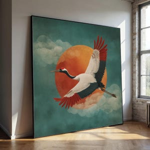 Könnte beinhalten: Großer gerahmter Kunstdruck mit einem fliegenden Kranich. Der Vogel hat weißes, schwarzes und rotes Gefieder, vor einem türkisfarbenen Hintergrund mit einer großen orangefarbenen Sonne und flauschigen Wolken. Das Kunstwerk wird in einem modernen Innenraum gezeigt.
