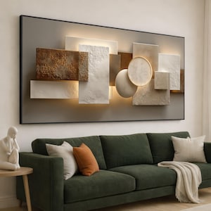 Puede incluir: Arte mural abstracto con formas geométricas rectangulares y circulares en tonos blancos, marrones y beige. Enmarcado en negro, se ilumina con luz cálida, creando una estética moderna. Se encuentra sobre un sofá verde.