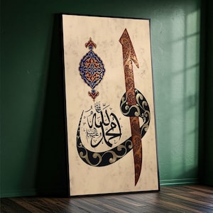 May include: Framed artwork with Arabic calligraphy in black and gold, and a decorative pendant in blue, red, and gold. The background is a textured beige, and the frame is black. The artwork leans against a green wall.