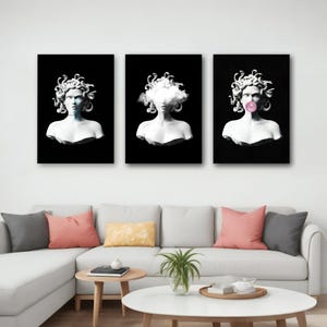 May include: Triptych of Medusa busts on black backgrounds. The busts are white, with snake-like hair. One has a cloud in place of a face, and another has a bubblegum bubble. The art is displayed above a white couch with colorful pillows.